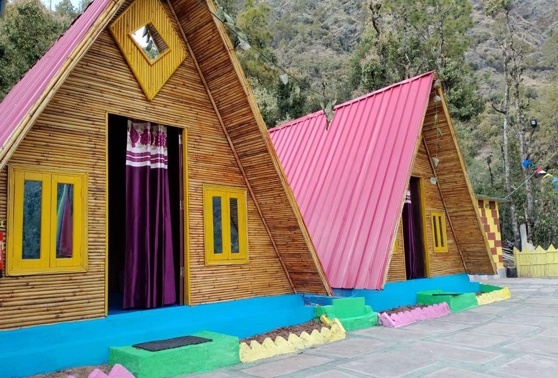 Two colourful bamboo A-frame huts with pink roofs